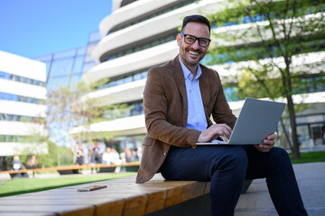 Portrait of happy male entrepreneur working on project over wireless computer while sitting on bench
