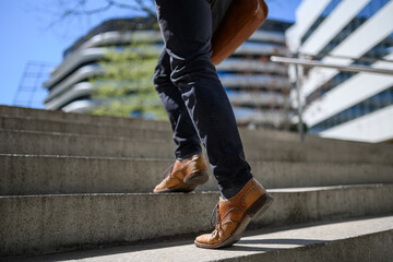 Low section of young businessman wearing leather shoes walking on steps against building in city