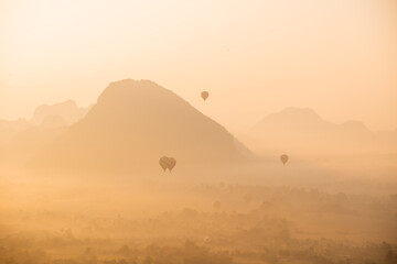 hot air balloons rising at sunrise in the mountain valley in Vang Vieng, the adventure capital of...