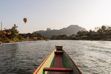 boat going down the river towards mountains and hot air balloon in Vang Vieng, the adventure...