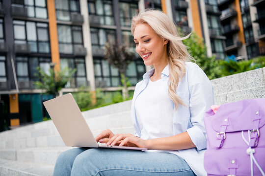 Photo of rest time young woman doing homework using netbook macbook pro air with good battery condition sitting outdoors city buildings