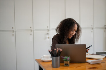 A woman is sitting at a desk with a laptop and a cell phone. She is smiling and she is enjoying her...