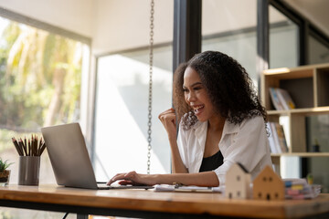 A woman is sitting at a desk with a laptop and smiling. She is happy and enjoying her work
