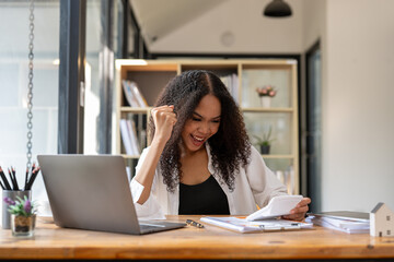 A woman is sitting at a desk with a laptop and a calculator. She is smiling and she is happy