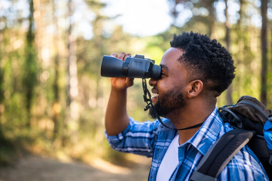 Young man enjoys using  binoculars and hiking  in nature. - Powered by Adobe