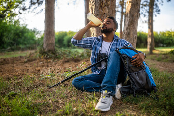 Young hiker drinking energy drink while enjoys resting in nature.