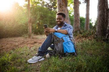 Young hiker using mobile phone while enjoys resting in nature.
