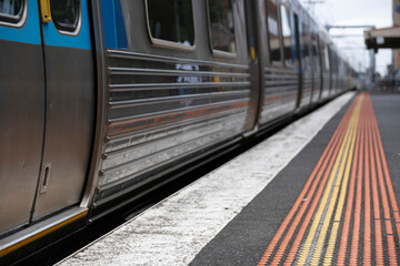 Fototapeta premium Railway station platform with yellow and red safety dots, and a departing PTV metro train in Melbourne, Australia. Focus on the dots in front and the doors at the left