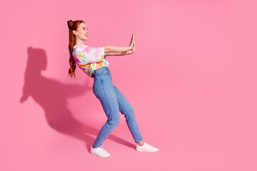 Full size photo of positive girl dressed colorful blouse jeans hold palms say stop look empty space isolated on pink color background