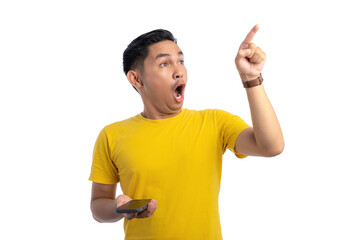 Shocked young Asian man holding mobile phone and pointing finger in the air with amazed expression isolated on white background