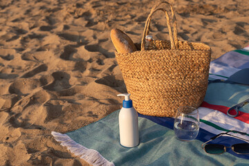 Sun screen cosmetic bottle with jute bag on striped beach towel on the sand. Summer vacation lifestyle concept