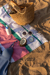 Jute beach bag, sunglasses, sun screen cosmetic bottle and swimsuit on the striped towel on the sand. Summer vacation lifestyle concept