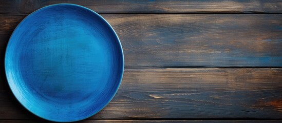 A blue plate rests on a wooden surface seen from above The wood s texture adds depth to the image leaving ample space for your creative design