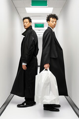 Two men in suits and coats pose for a photo in a hallway