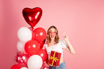 Photo portrait of lovely woman balloons sunglass hold gift v-sign dressed stylish white garment hairdo isolated on pink color background