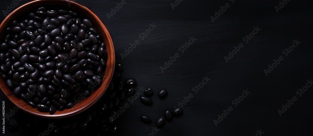 Poster a black bowl filled with black beans is seen from above on a black background in this copy space ima