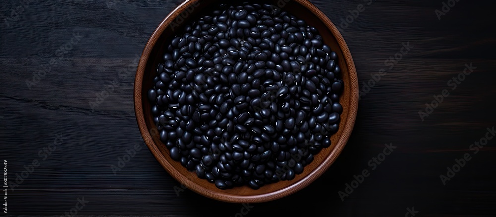 Poster a black bowl filled with black beans is seen from above on a black background in this copy space ima