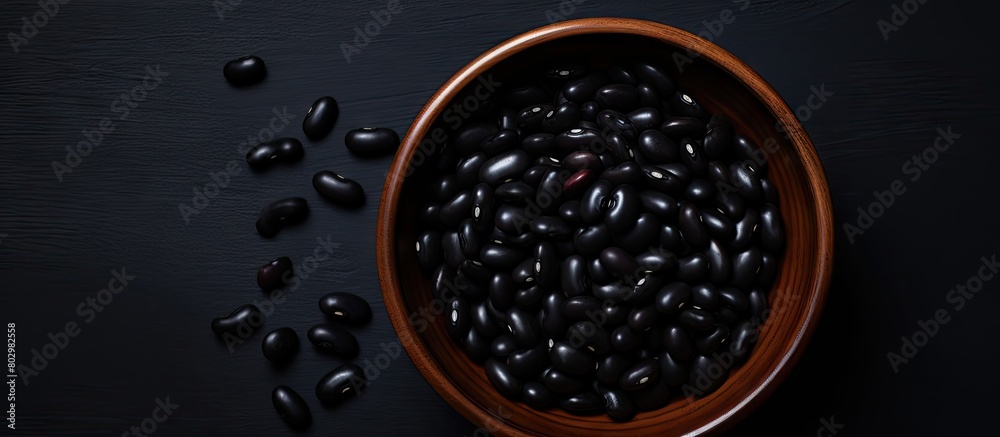 Aufkleber a black bowl filled with black beans is seen from above on a black background in this copy space ima
