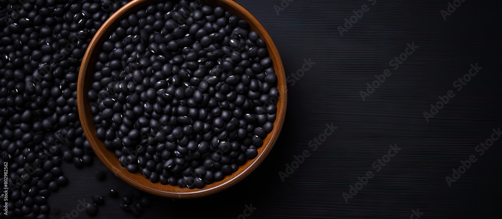 Poster A black bowl filled with black beans is seen from above on a black background in this copy space image