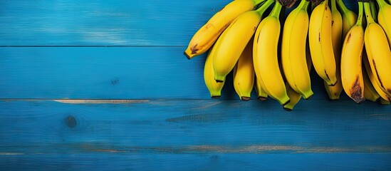 A copy space image of yellow ripe bananas resting on a vibrant blue wooden table - Powered by Adobe