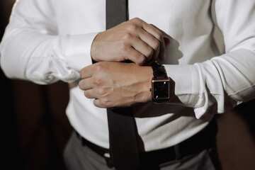 A man is wearing a watch and a black tie. He is adjusting his tie and his hands are visible
