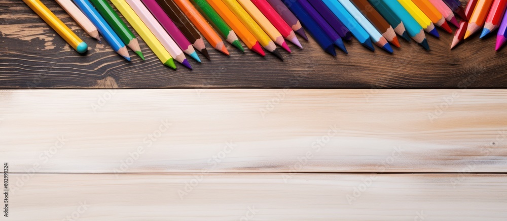 Poster a copy space image of a white sheet of paper and six crayons placed on a wooden desk representing th