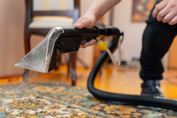 close up in the apartment a master cleaner waters the carpet with detergent from a professional...