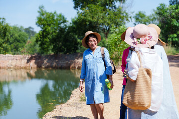 A single traveler, cheerful in blue, strolls waterside, friend engages from behind, sunhats a nod...