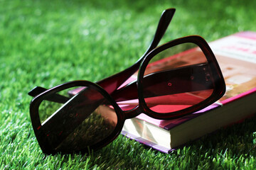 Women's sunglasses and book on the grass in the garden