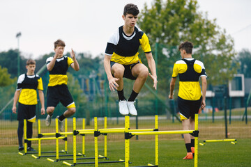 Young teenage boys jumping over hurdles during summer training camp. Players in soccer training. Youth football team preparing for the season start