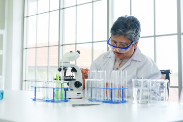 Senior Asian female science teacher, Concentrated middle-aged researcher in lab coat adjusting...