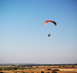 Silhouette of a man flying a motorized paraglider in the blue sky over a flat landscape. Extreme...
