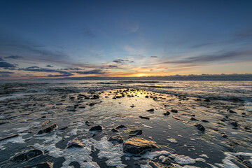 The stones of the pier emerge as the North Sea recedes during a colorful sunset. The peak of the...