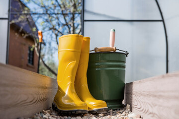 Yellow rubber boots, a bucket and a small shovel in the new greenhouse. The concept of spring...