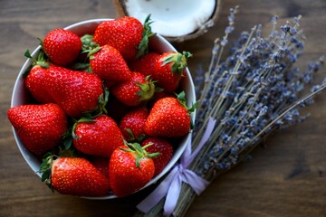 a plate of strawberries stands on a wooden table against a background of coconut and lavender