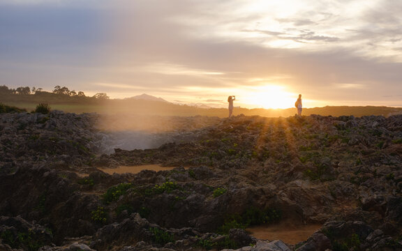 Two people taking photos at sunset on a rugged coastline