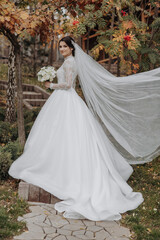 A bride is walking down a path wearing a white dress and a veil. She is holding a bouquet of flowers
