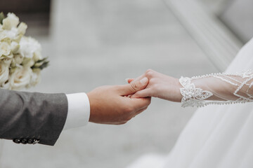 A bride and groom are holding hands, with a bouquet of flowers in the bride's hand