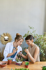 Two women, sharing a moment at a table surrounded by plants in an art studio.