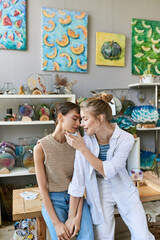 Two women, a loving lesbian couple, admire paintings in an art studio.