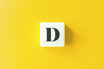 Capital Letter D. Text on Block Letter Tiles against Yellow Background.