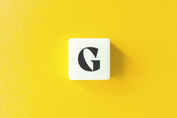 Capital Letter G. Text on Block Letter Tiles against Yellow Background.