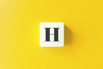 Capital Letter H. Text on Block Letter Tiles against Yellow Background.