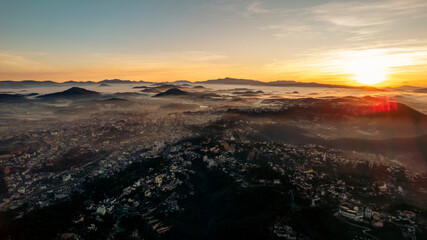 An aerial view of Da Lat city nestled among green hills, with a lake in the foreground.