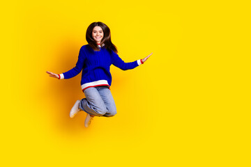 Full length photo of pretty teen girl jumping have fun wear trendy knitwear blue outfit isolated on yellow color background