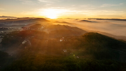 The morning sun peeks through the fog over rolling hills, casting long shadows across the landscape.