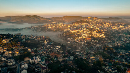 Aerial view of Dalat City at sunrise, showcasing urban landscape amidst natural beauty, buildings...