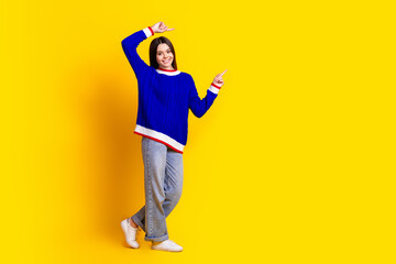 Full length photo of pretty teen girl point empty space wear trendy knitwear blue outfit isolated on yellow color background