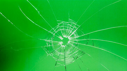 A hole with cracks in the glass. Broken window on a green background - obrazy, fototapety, plakaty