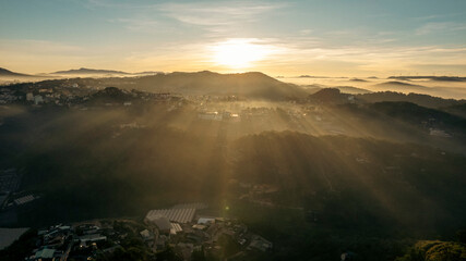 Aerial view of Da Lat at sunrise, showcasing mist-covered buildings amidst lush mountains, under a...